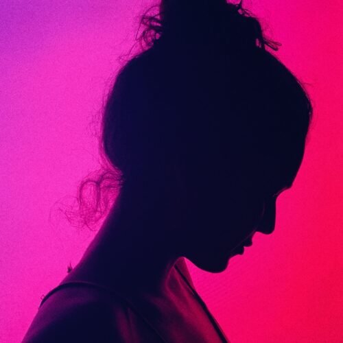 Side view of crop anonymous melancholic female with bun on head near colorful wall